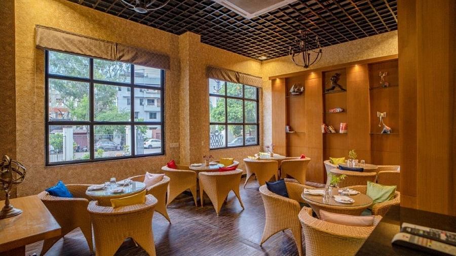Dining area with wooden furniture and large glass windows at Golden Tulip, Udaipur.