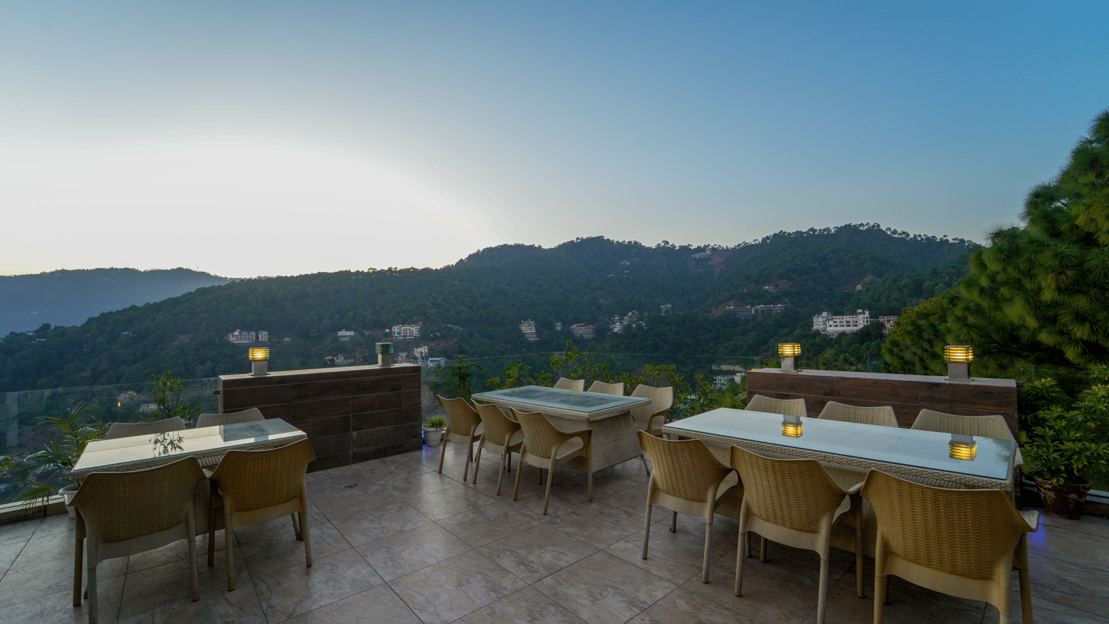 An overview of the terrace-top dining area with chairs and tables with the backdrop of the mountains at our Kasauli Hills Resort - DLS Whispering Winds, Kasauli.