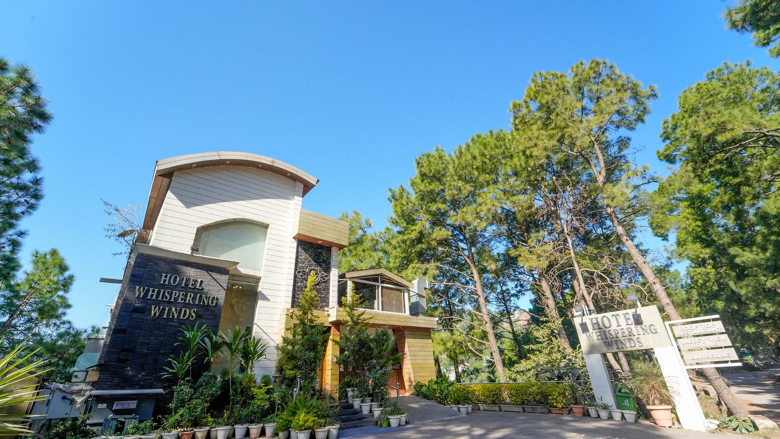 A facade image of DLS Whispering Winds surrounded by trees and greenery