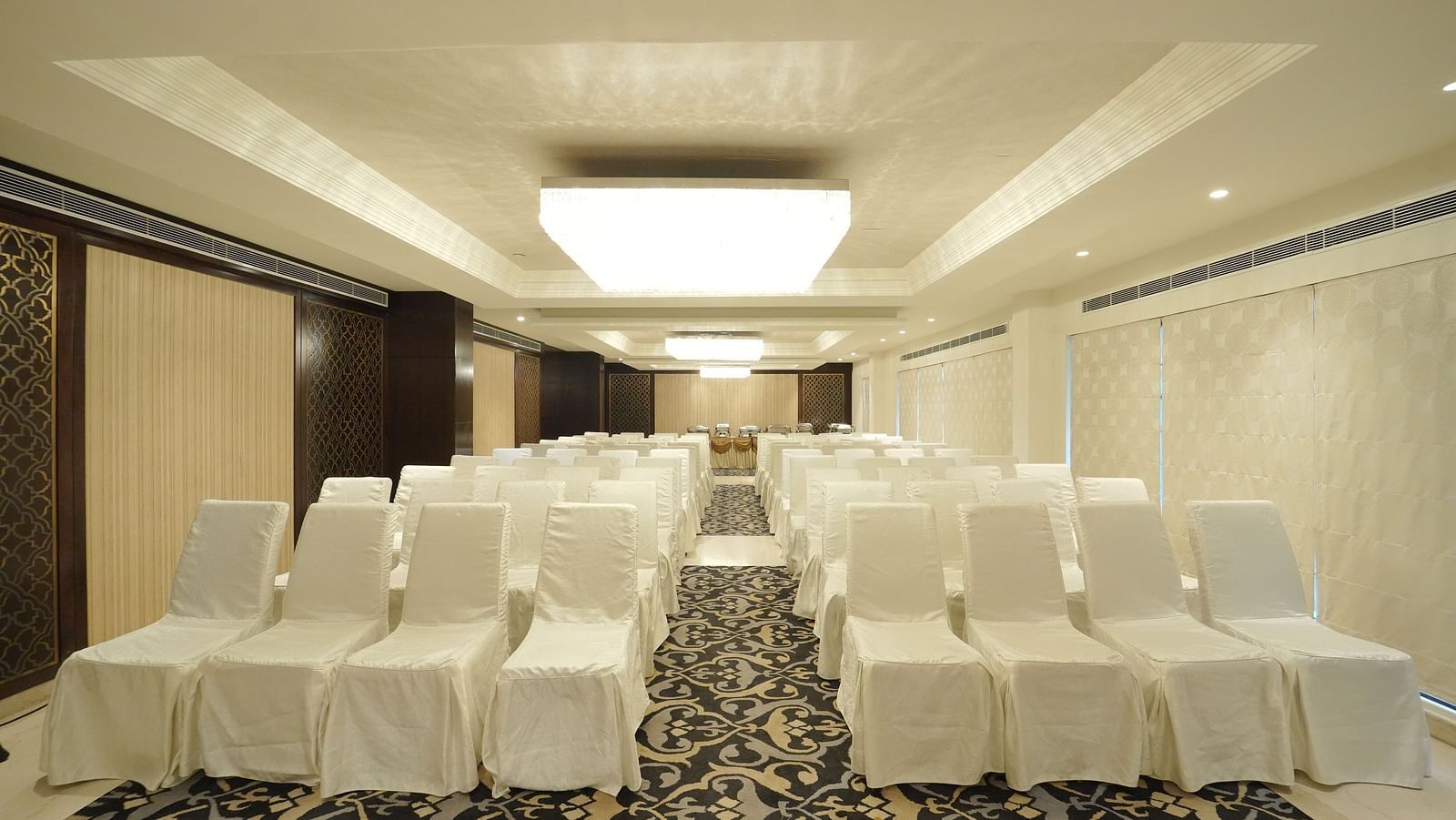 A spacious event hall with many chairs covered in white fabric, arranged on a patterned carpet - Fragrant Nature Cochin