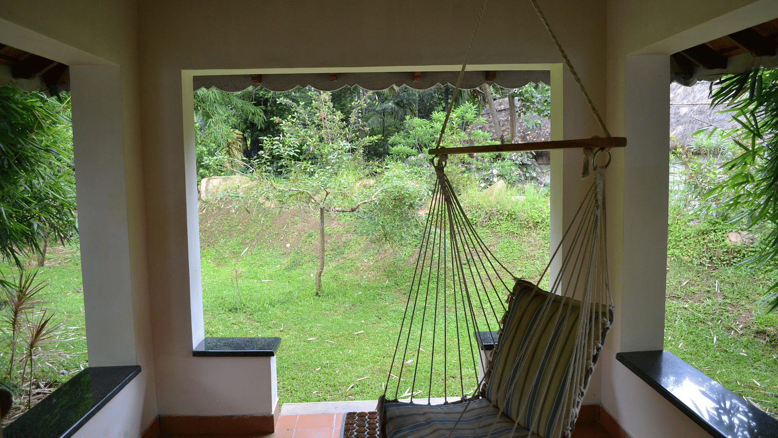a cot inside a small shed with gardens outside - Kadkani River Resort, Coorg