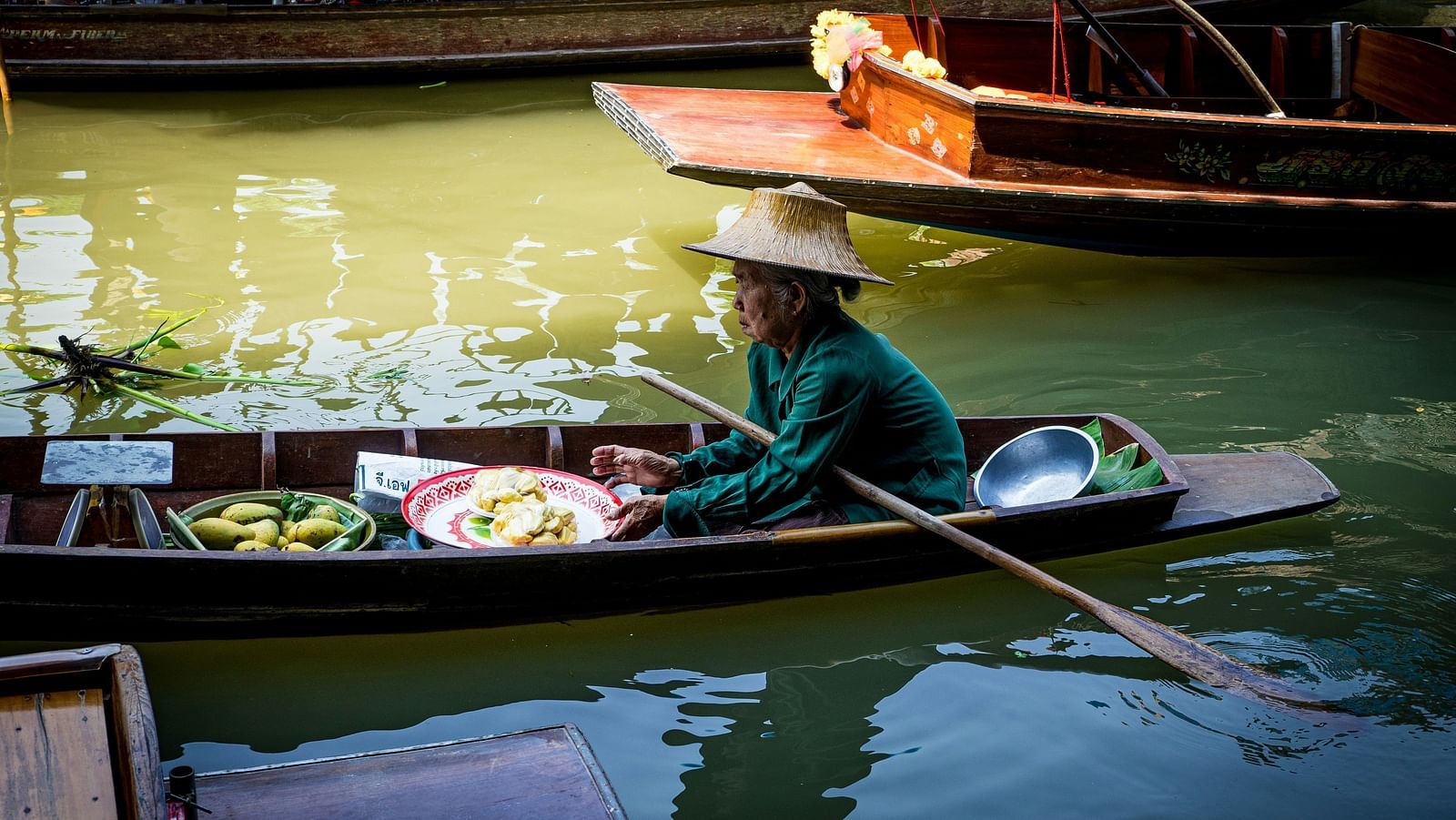 an image showcasing a woman on Floating Markets of Damnoen Saduak with other boats behind her boat