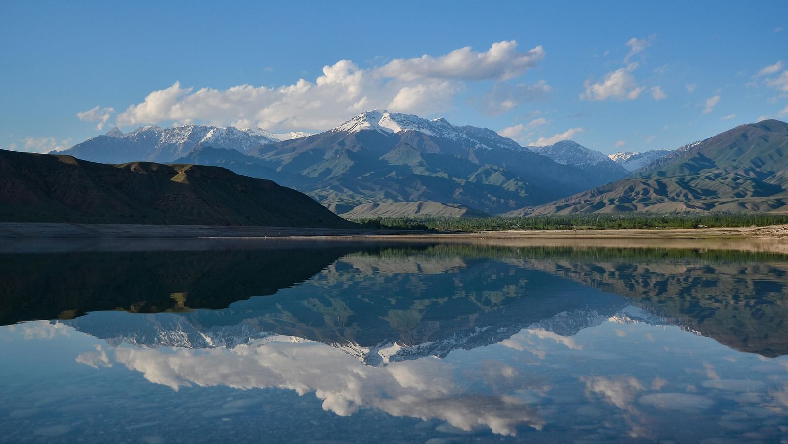 An image captures stunning mountains with a serene lake in the foreground, reflecting their beauty, creating a picturesque scene