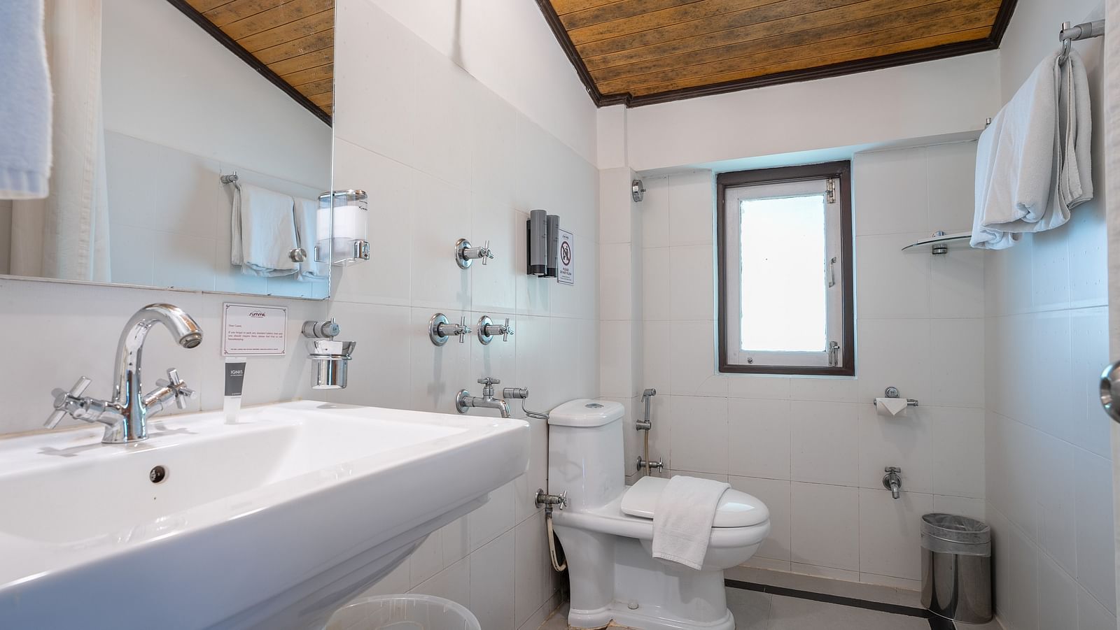 In the Deluxe Room, there is a spacious bathroom with a washbasin topped by a mirror, and neatly arranged towels for showering at Summit Norling Resort & Spa, Gangtok