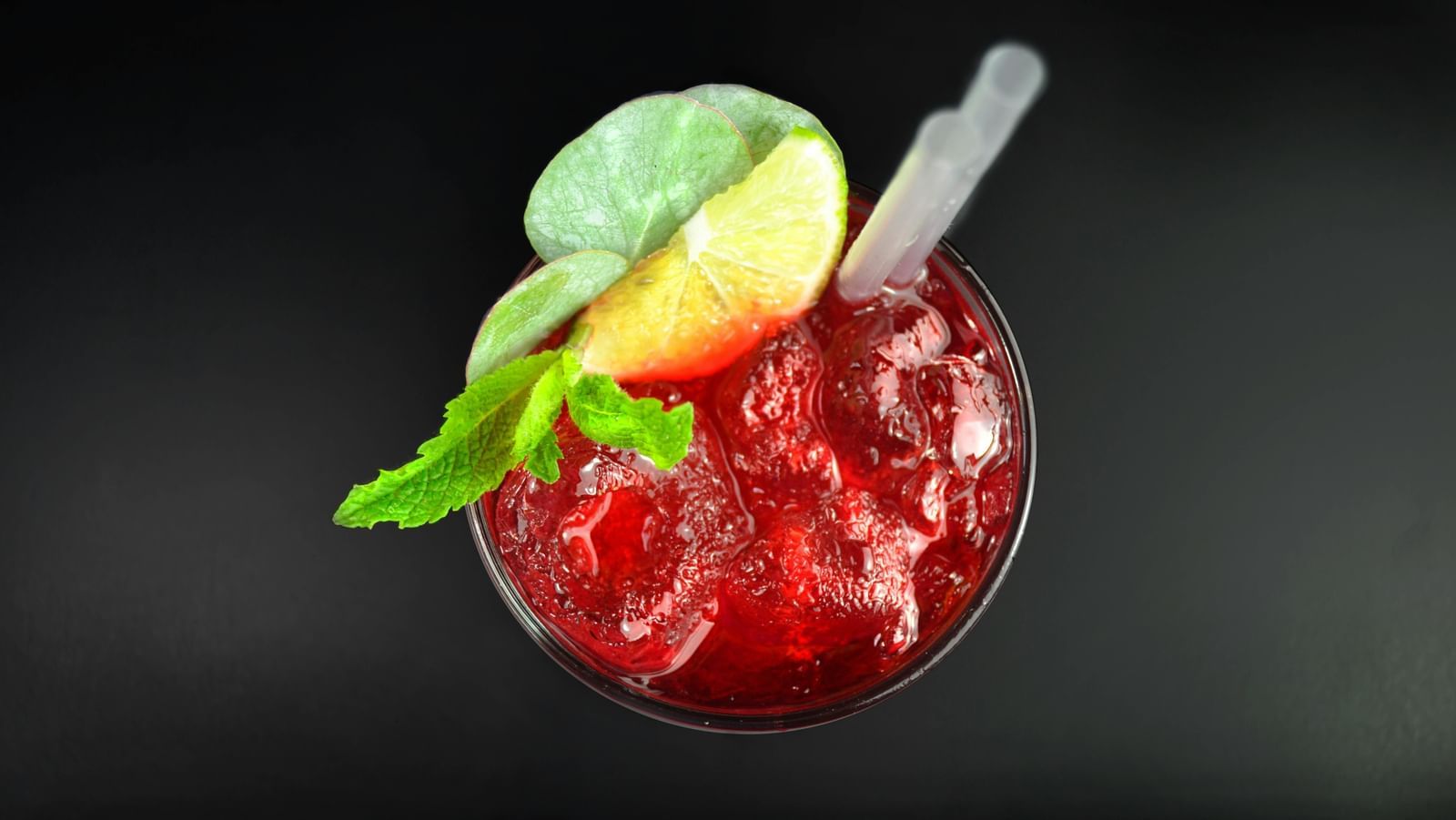 A pink iced drink in a glass, garnished with a lemon wedge and mint leaves.
