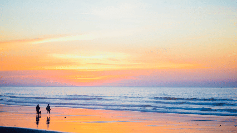 Two people strolling along the beach at sunset, enjoying the colourful and serene coastal view.