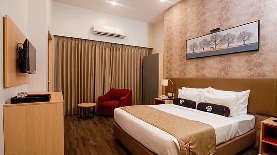 a plush bed with warm toned interiors and room amenities - Mastiff Hotel, Ankleshwar