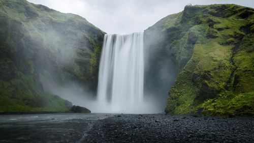 An overview of a waterfall cascading down to a waterbody with rocks covered in moss next to it