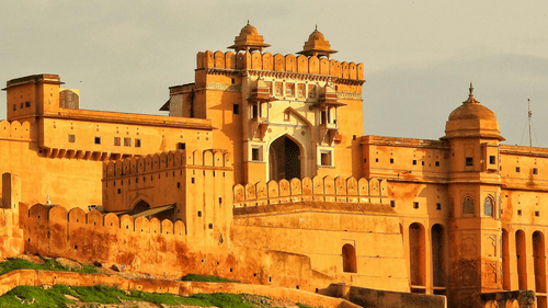 The golden sandstone facade of a fort gate stands under a soft, hazy sky during the late afternoon.