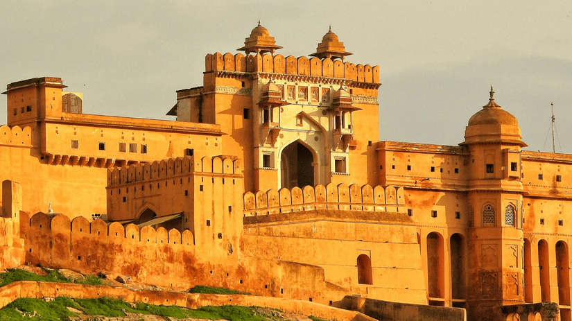 The golden sandstone facade of a fort gate stands under a soft, hazy sky during the late afternoon.