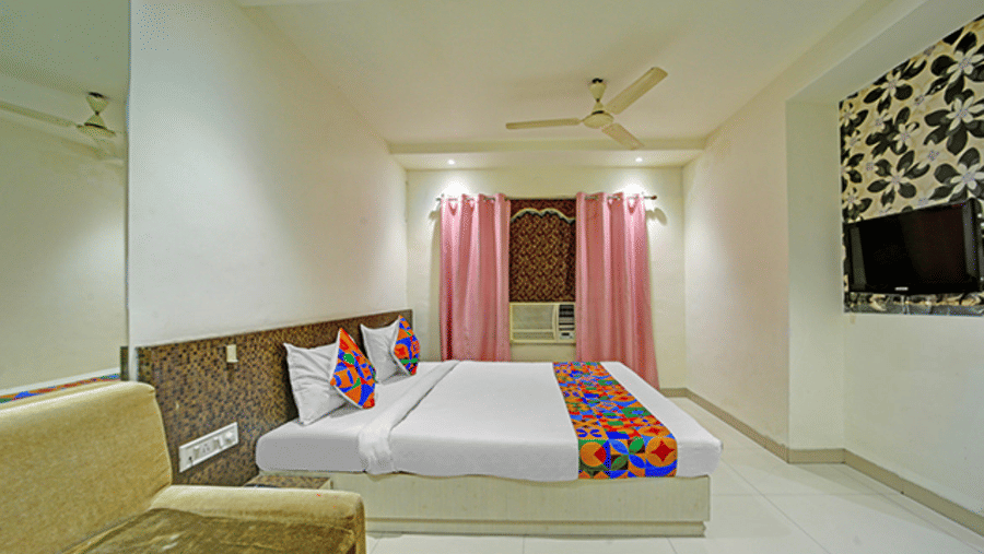 Spacious room with double bed, sofa, wall art panel and window with pink curtains at Hotel Maurya, Bhopal.