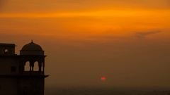 A silhouette of Tijara Fort-Palace in Alwar is seen against a vibrant orange and yellow sunset sky.