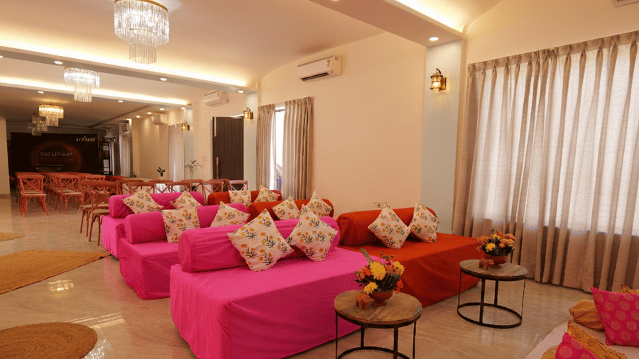 Event hall with chandeliers, lounge seating, and curtained windows at Grassfield Riviera Resort, a wedding venue near Jaipur.