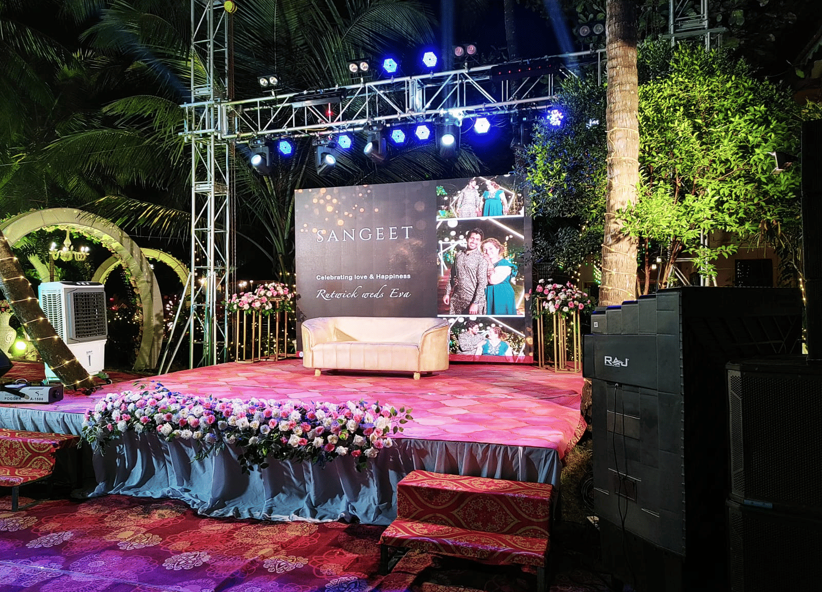 Outdoor stage with floral decorations and LED screen set against palm trees at Paradise Lagoon Resort, Udupi.