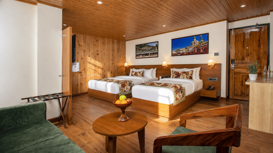 2 double beds set against a wooden headboard, lamps, wall pictures, and a door at Valmere Lungta Boutique Hotel & Spa, Darjeeling.