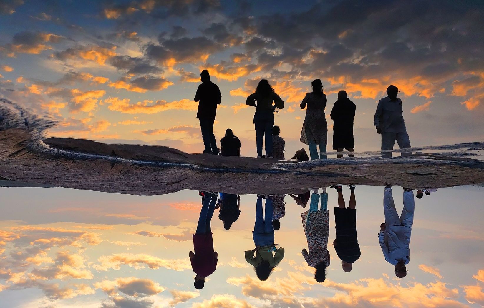 People's silhouettes reflected in water against sunset.
