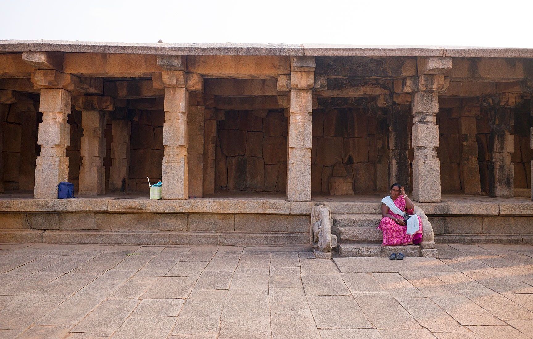 Ancient hampi stone corridor with a woman seated on the steps
