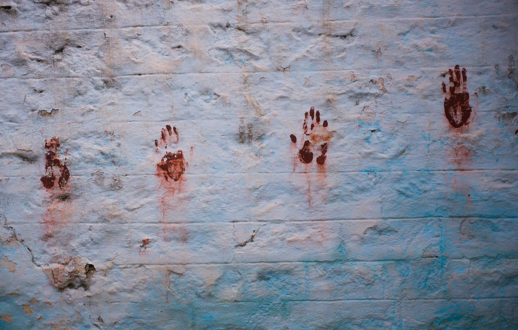 Multiple reddish-brown handprints on a light wall.