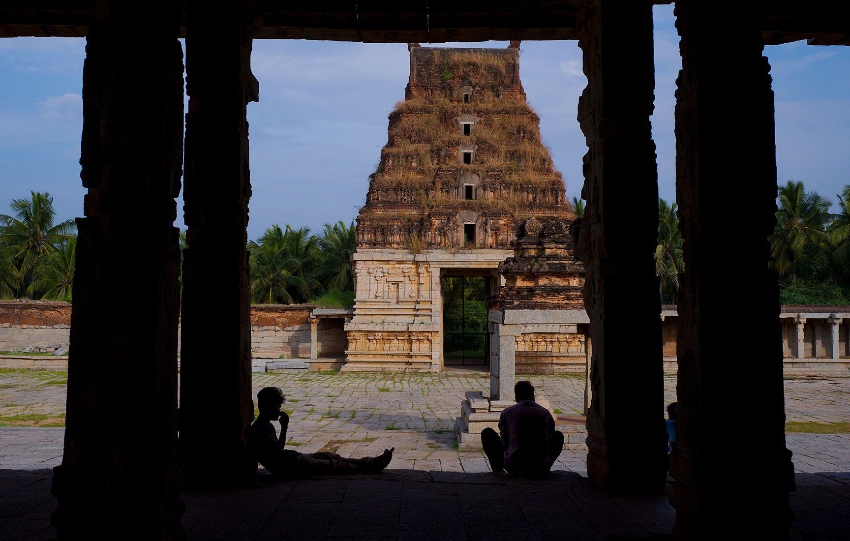 Silhouetted visitors in temple pavilion viewing an ancient gopuram