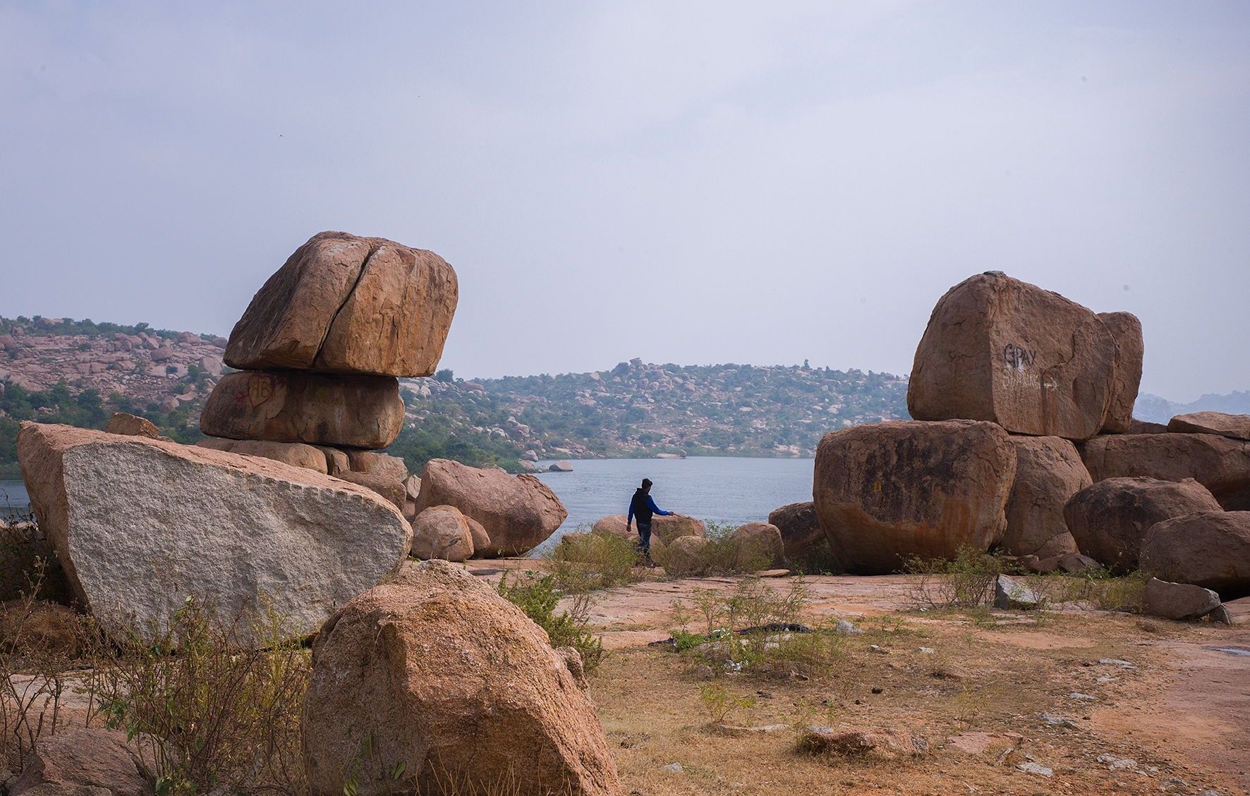Visitor walking among massive balancing granite boulders by the Tungabhadra River at Hampi
