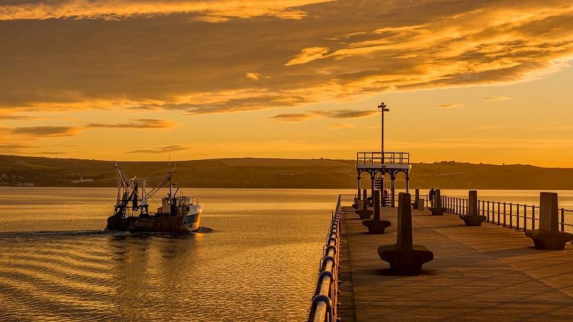 A boat leaving from pier at sunset