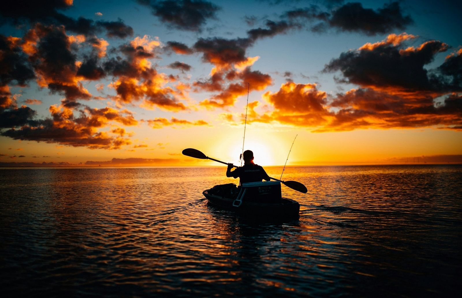 Silhouette of a kayaker paddling on a calm sea at sunset.