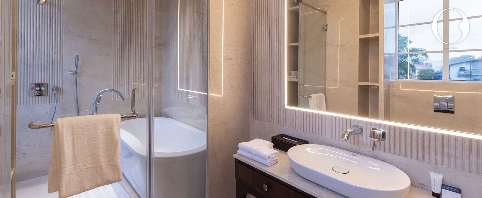 Full view of the bathroom with a wash basin along with a bath area separated by a transparent glass door at Miros Hotels.