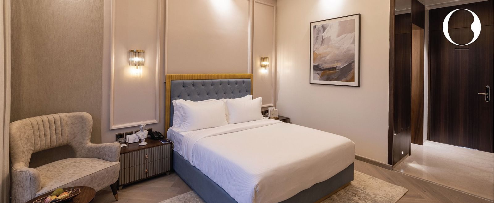The Serene Room with modern interiors with an arm chair and a double bed along with the entrance corridor in the corner at Miros Hotels.