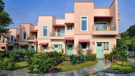 Exterior view of Lion's Den at Karma Chalets building during the day, showing pink walls, balconies, and a garden with a pathway.