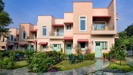 Exterior view of Lion's Den at Karma Chalets building during the day, showing pink walls, balconies, and a garden with a pathway.
