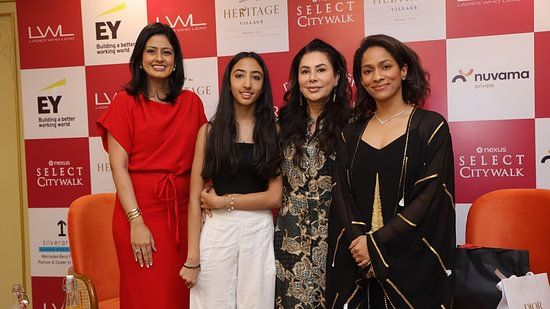 Four women posing at a corporate event, featuring branding from prominent companies like EY and Navitas.