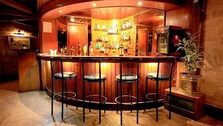 Bar with tall chairs and tables, featuring a dark-themed setup for guests to enjoy their drinks.
