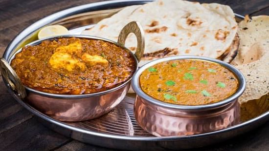 Traditional North Indian thali with curries and Indian breads in copper bowls.