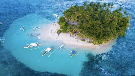 High-angle shot of a small tropical island with white sand and boats in clear blue water at Lamari Siargao.
