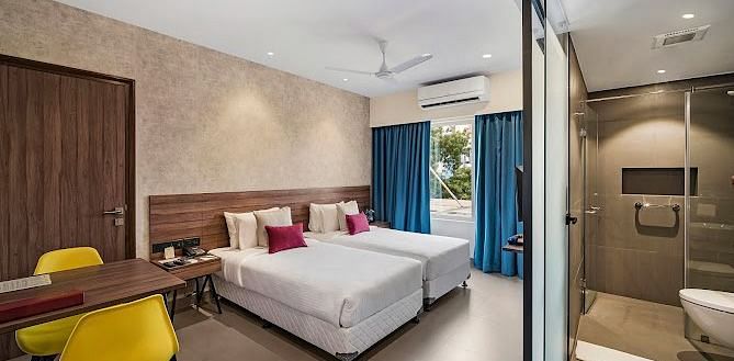 One of our rooms in thoothukudi with twin beds, a table with yellow chairs, and a modern shower area in front - Regency Tuticorin by GRT Hotels