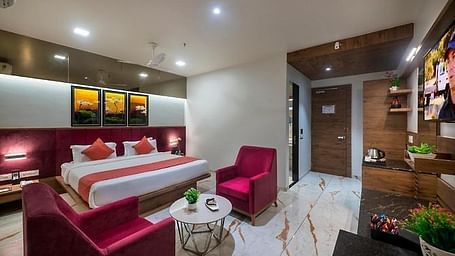 A room featuring a neatly made bed, a seating area, and a dressing table at Angel Lords Eco Inn Amreli.