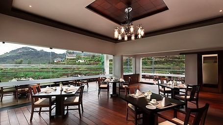 Shot of a restaurant full of tables, chandelier and a big window with mountain in the background.