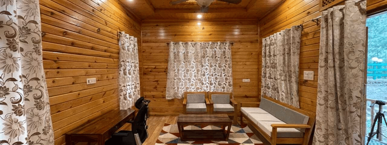 A living room at Dawat e Drung by FrozenFall Resort, Drung, Tangmarg, featuring a sofa, a coffee table, a writing desk with a chair and curtains.