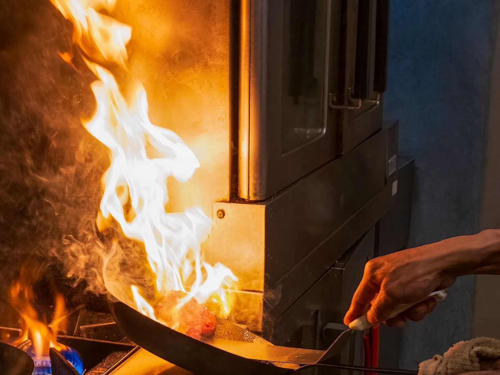 Chef flambéing a dish with open flames in a busy kitchen at The Groveland Hotel.
