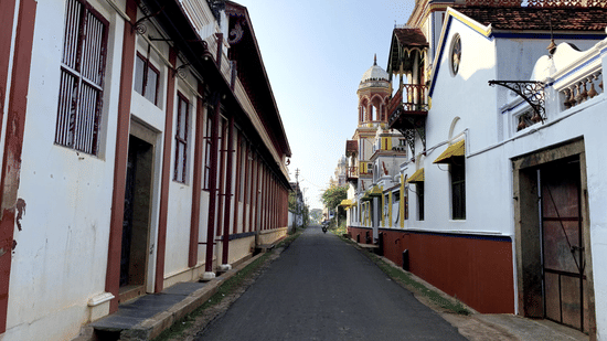 A narrow, paved street stretches between traditional white and red buildings with wooden frames and small balconies under a clear sky.