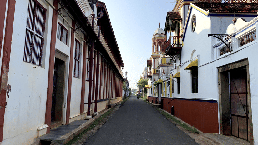 A narrow, paved street stretches between traditional white and red buildings with wooden frames and small balconies under a clear sky.