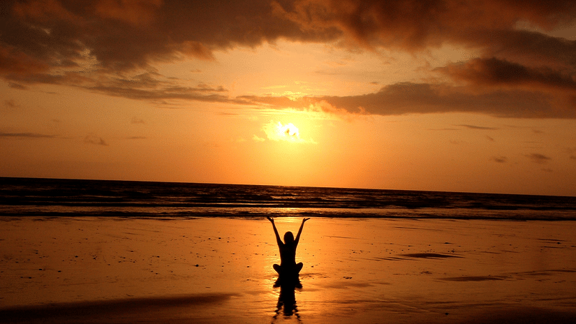a woman doing beachside yoga near the overlapping waves and the sun setting in the background - Azaya Beach Resort Goa
