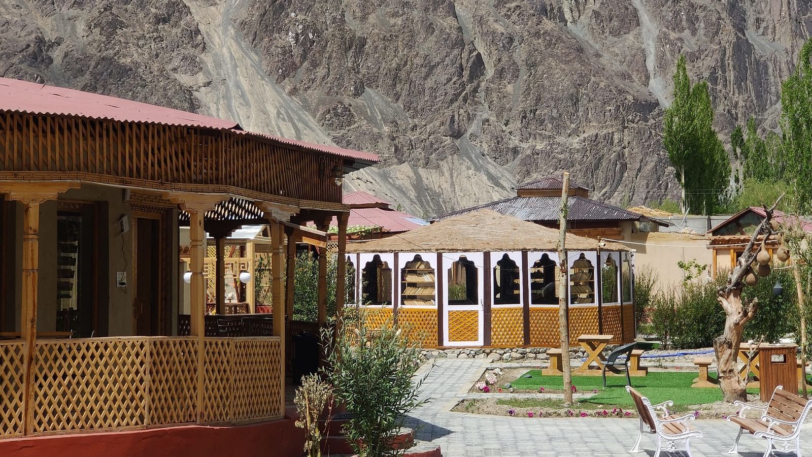Outdoor seating area and traditional wooden structures with mountain backdrop, featuring a garden path and part of a circular blue-tiled pool.