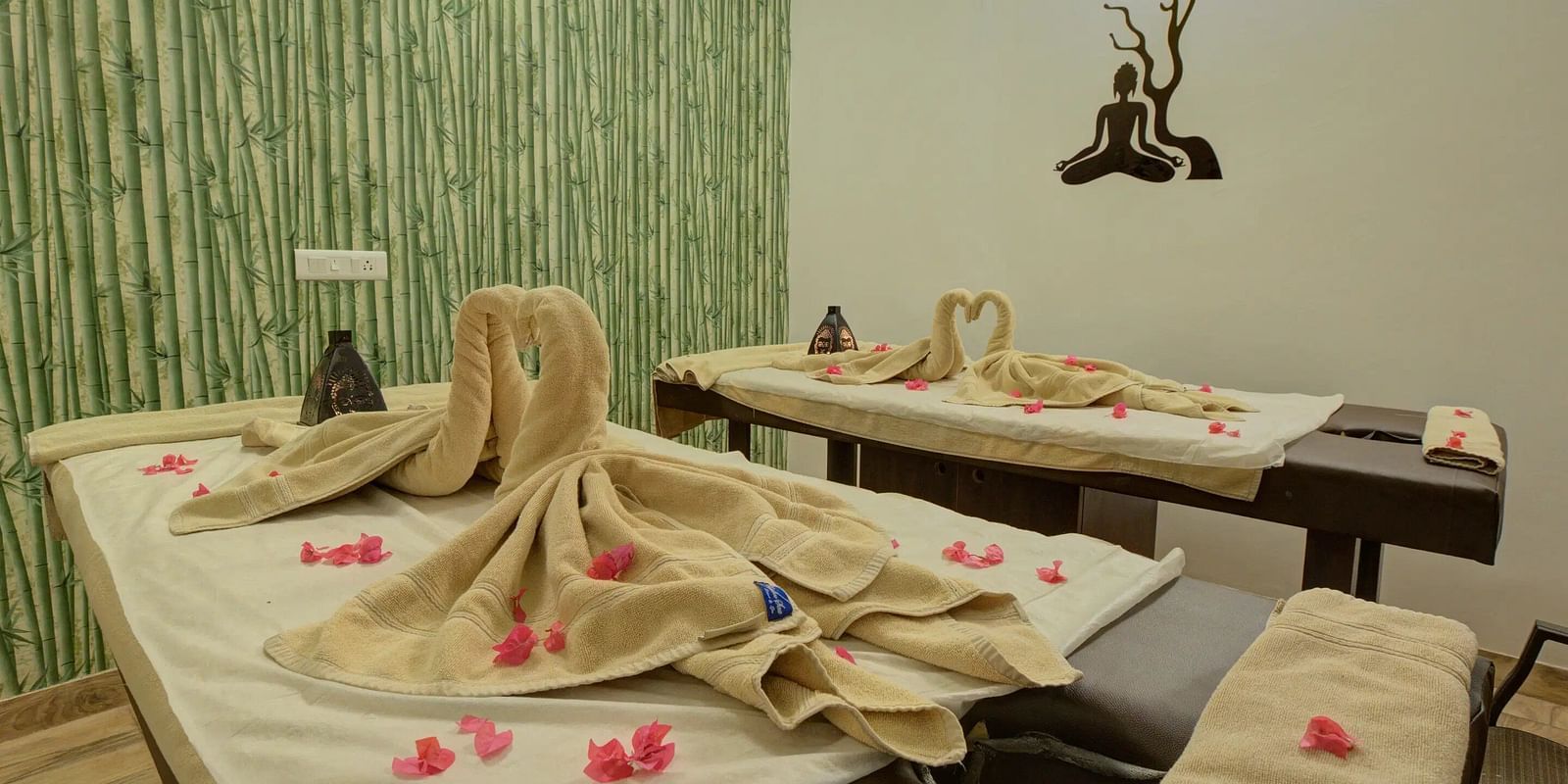 Cosy spa room with two massage tables, folded towels, rose petals, and a bamboo-themed wall. - Bamboo Saa, Udaipur