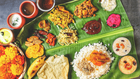 Traditional South Indian meal served on a banana leaf with rice, curries, chutneys, papad, sweets and assorted side dishes.
