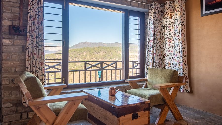 Seating area featuring wooden furniture, floral curtains, and a stunning valley view through a window. - Blusalzz Homes The Himalayan Bungalow, Almora