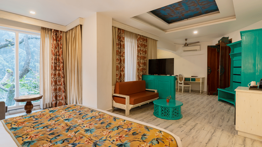 A spacious suite featuring a bed with a floral runner, a multi seater sofa, a wardrobe, a television unit, and a writing desk with a chair | Summit by the Ganges Beach Resort & Spa, Rishikesh