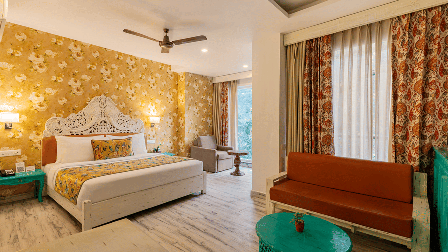 A well-lit suite featuring brightly coloured furniture, an accent wall, full length curtains, and an attached balcony | Summit by the Ganges Beach Resort & Spa, Rishikesh