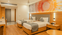 A vibrant twin room at Pride Elite Himmatnagar is highlighted by a colorful abstract art piece on the wall.
