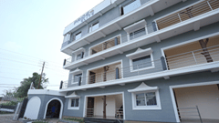 Exterior of Pride Elite Mandarmani with the Pride Elite signage, grey and white multi-storey facade, balconies with decorative tree sculptures, and a gated entrance.